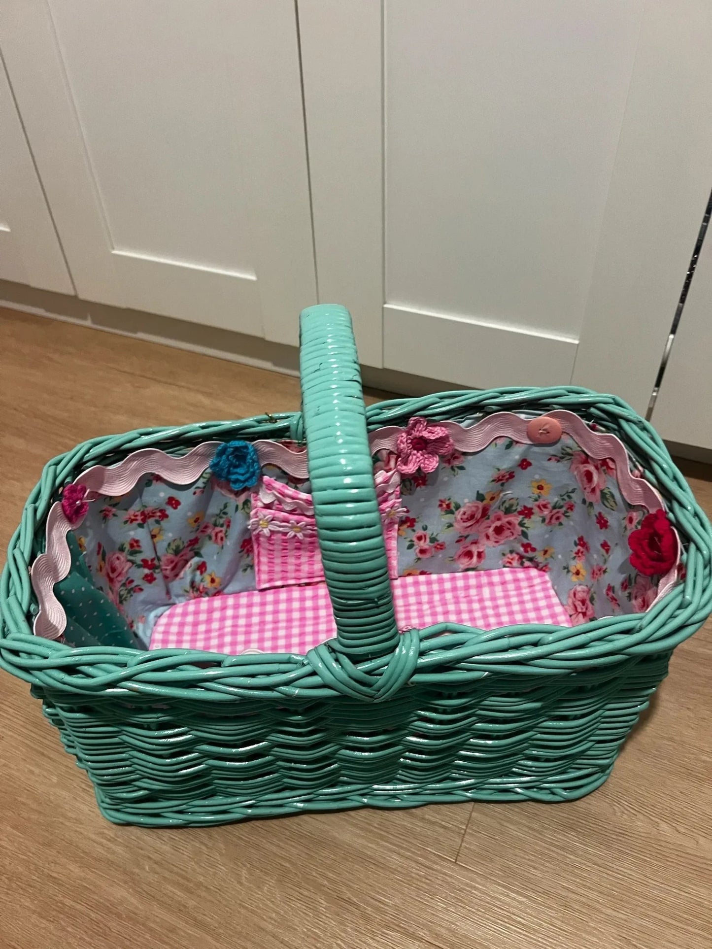 Picnic Girl teal wicker basket with floral lining and pink gingham base, featuring decorative crochet flower accents.